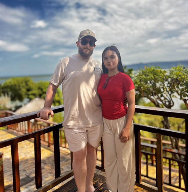 James and his fiancée standing together on a wooden deck overlooking the water